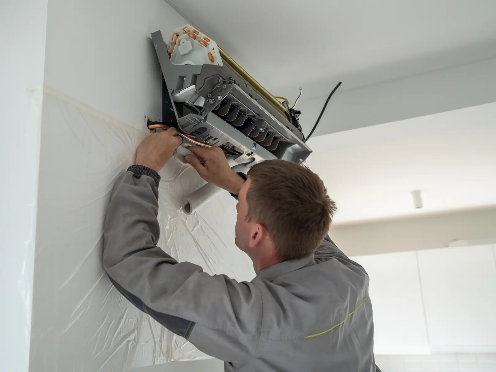 Installateur fixant un split mural de climatisation au mur d'un séjour