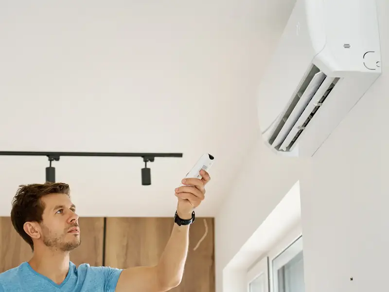Préparer sa climatisation avant l'été : le calendrier et les vérifications 2 Personne remettant en marche sa climatisation murale avec la télécommande